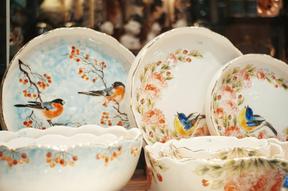 Editor arranging handmade stoneware plates and vintage glassware on a sunlit dining table